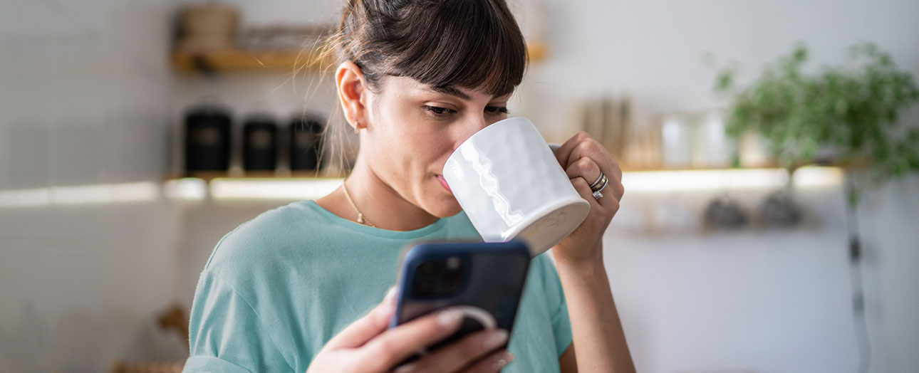 Eine Frau liest beim Morgen-Kaffee ihre Nachrichten auf dem Smartphone