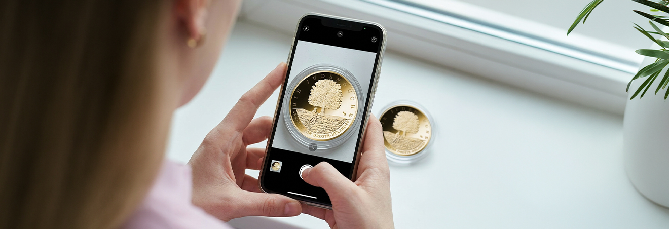 Abbildung eines Smartphones, das die Goldmünze „Die Judenbuche“ abfotografiert