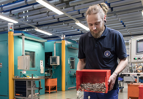 Ein Industriemechaniker schüttet Münzen aus einer kleinen Kiste in einen großen Transportbehälter.